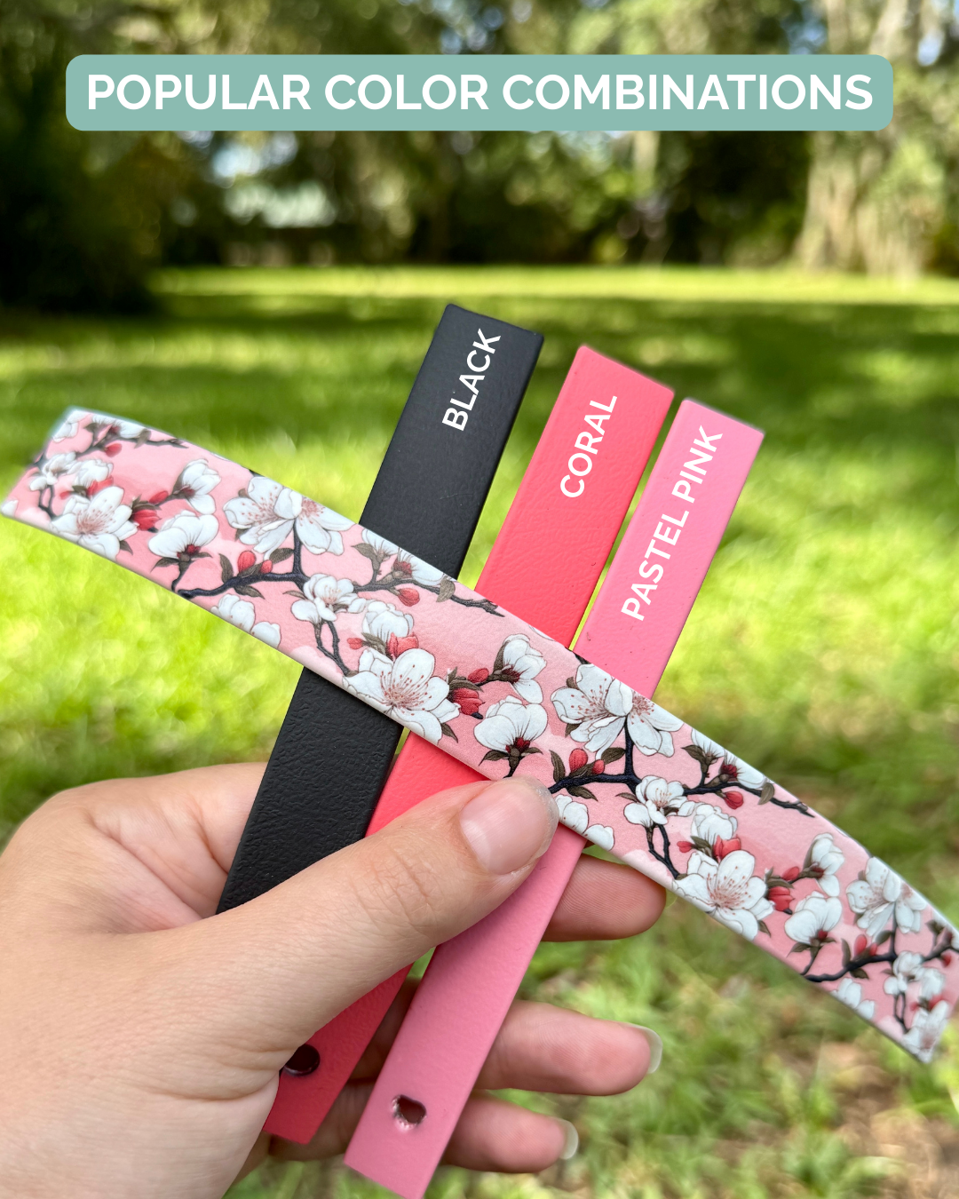 Hand holding color swatches with cherry blossom pattern, black, coral, and pastel pink labels against a blurred green outdoor background.