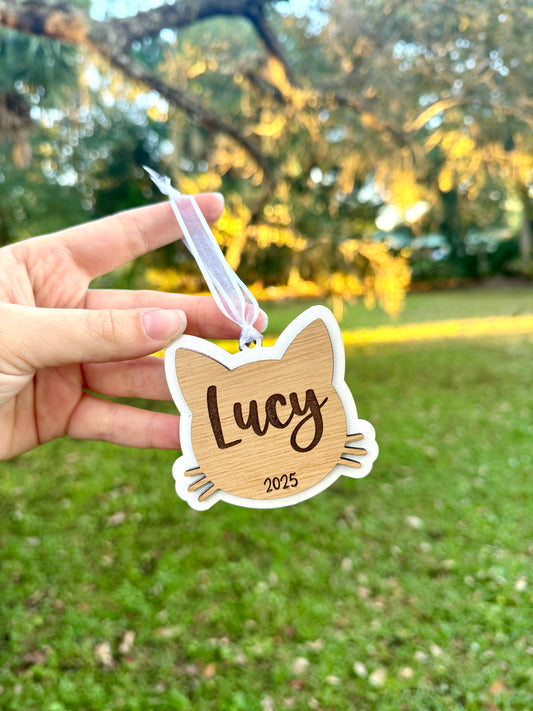 Hand holding a cat head shaped wooden cutout with 'Lucy' engraved.