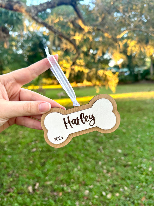 Hand holding a bone-shaped christmas Ornament with 'Harley' and '2025' printed on it.