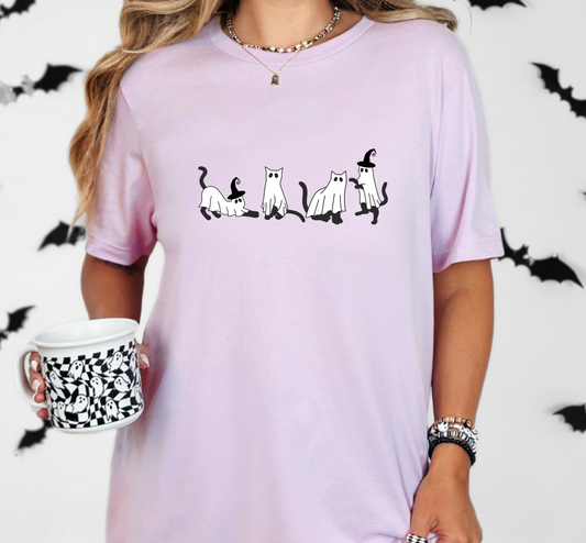 A person wearing a purple t-shirt with a graphic of 4 cats dressed as ghost on it. Two of the cats have witch hats on it. 