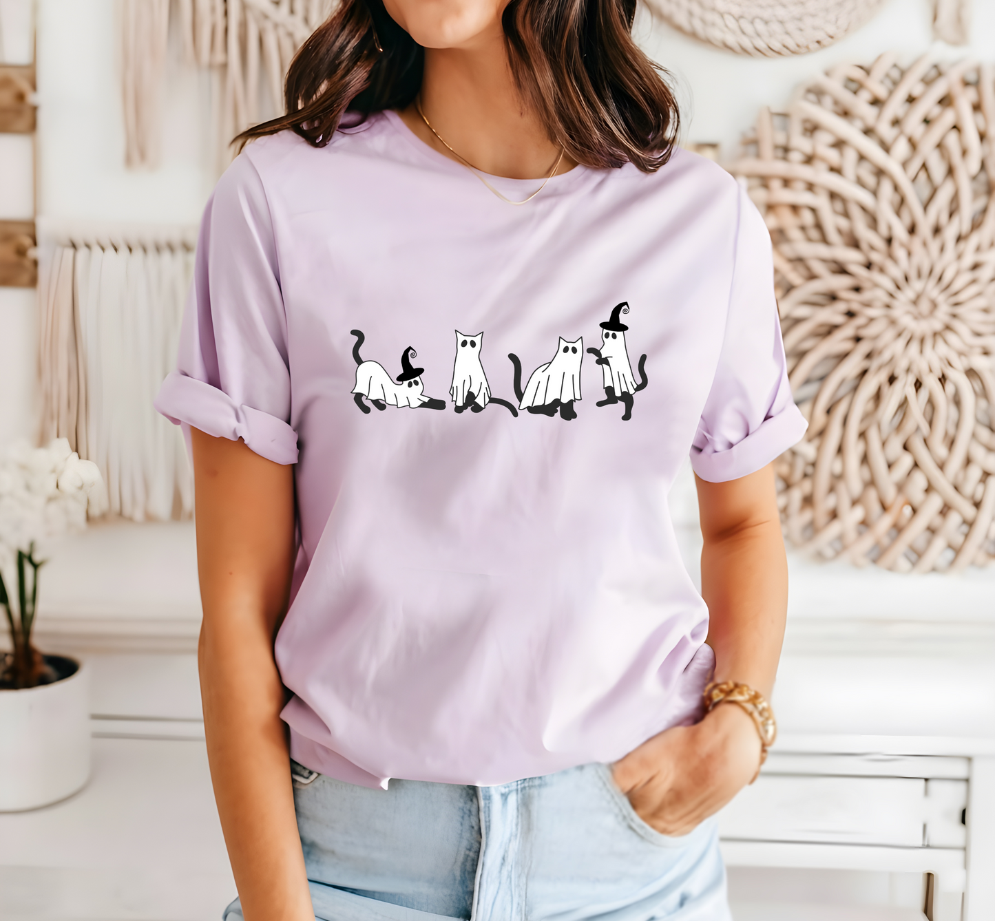 A person wearing a purple t-shirt with a graphic of 4 cats dressed as ghost on it. Two of the cats have witch hats on it. 