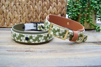 Two floral-patterned biothane collars on a wooden surface with a woven basket and plant in the background.