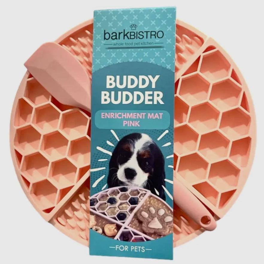 A pink and turquoise dog enrichment lickmat with a spatula, designed for pet use, displayed with its packaging which features a dog and the product name.