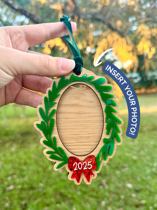 Wooden photo frame ornament with green wreath design held by a hand outdoors.