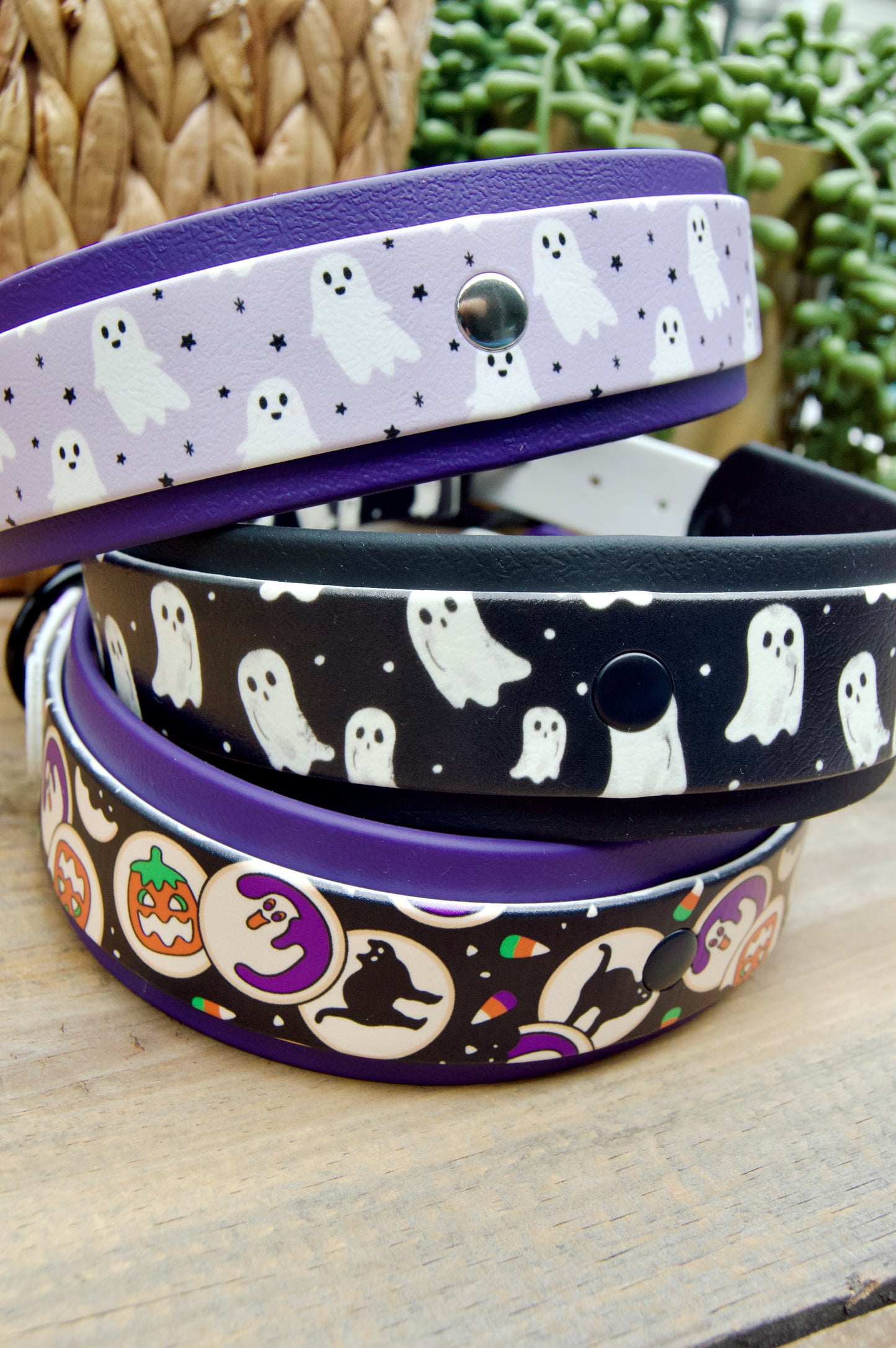 Three Halloween-themed biothane dog collars stacked on a wooden surface, Lilac Ghosts, Black and White Ghosts, and Halloween Cookies