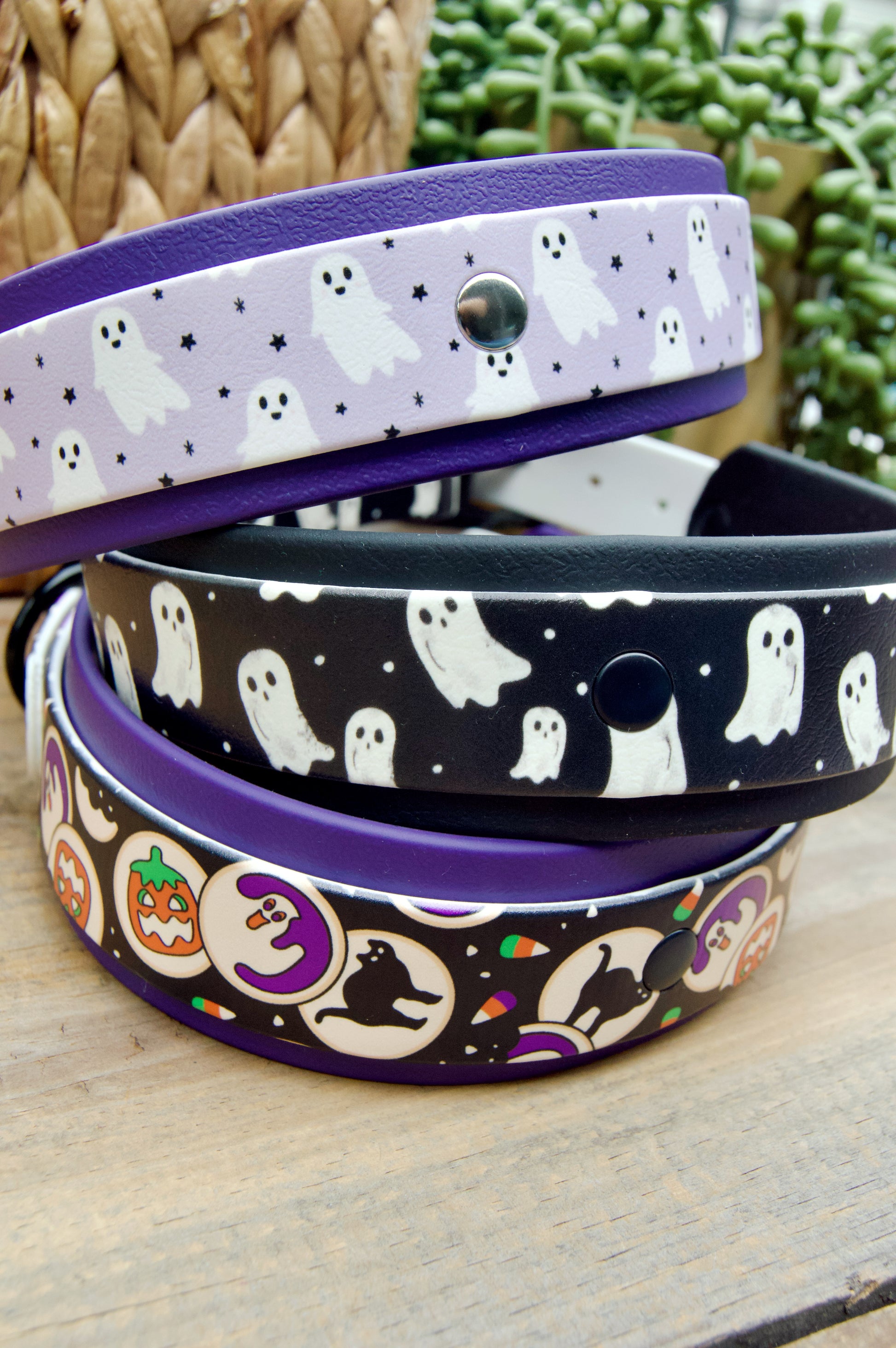 Three Halloween-themed biothane dog collars stacked on a wooden surface, Lilac Ghosts, Black and White Ghosts, and Halloween Cookies