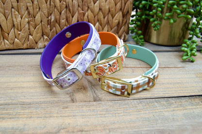 three Biothane collars from Fall and Halloween Collection, Lilac Ghosts, Pumpkins and Fall Plaid, stacked with wood background
