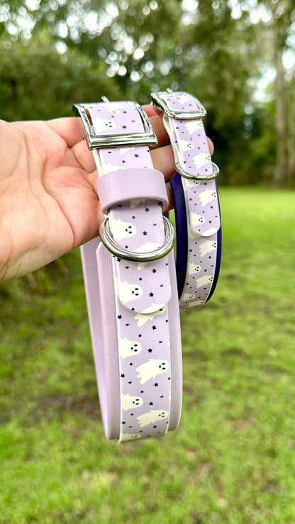 Two purple dog collars with ghosts and star patterns held by a hand against a green outdoor background.
