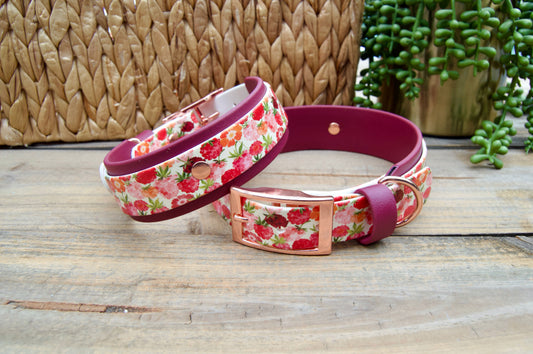 Two raspberry patterned dog collars on a wooden surface with a woven basket and plant in the background.