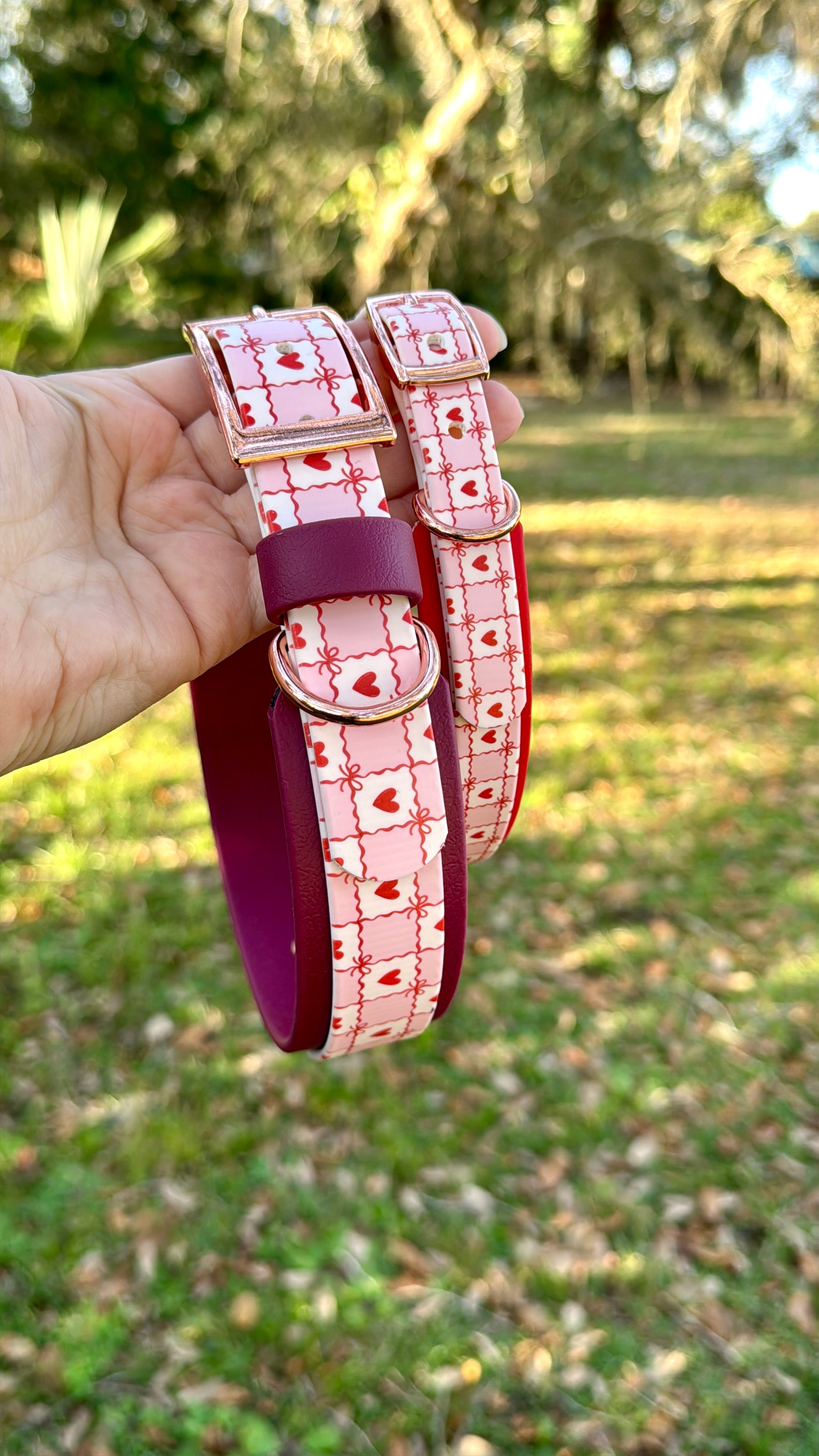 Pink and white checkered patterned biothane dog collar held in a hand with a grassy background