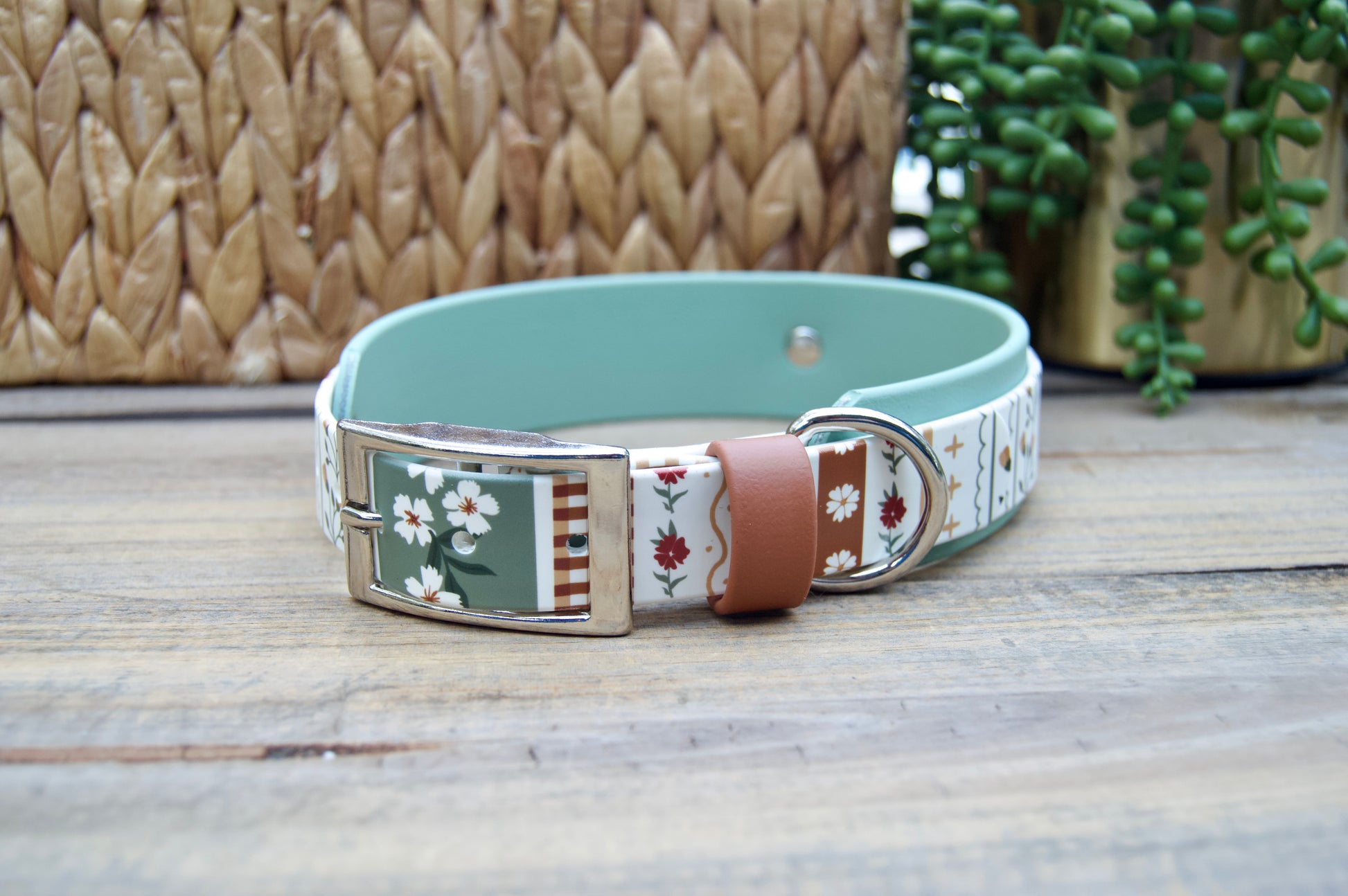 biothane dog collar with a striping floral design and sage green accent on a wooden surface with a natural basket and plant in the backgrounds