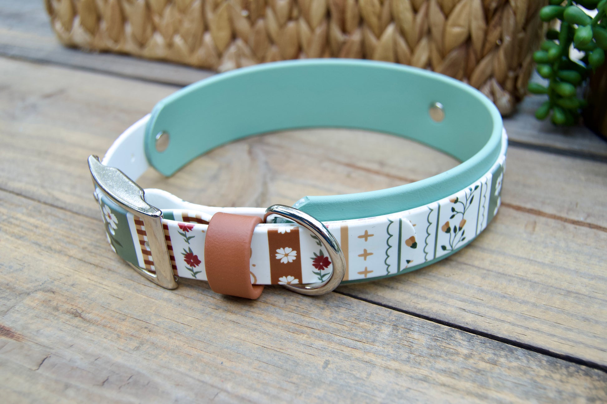 biothane dog collar with a striping floral design and sage green accent on a wooden surface with a natural basket and plant in the backgrounds