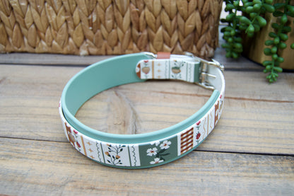 biothane dog collar with a striping floral design and sage green accent on a wooden surface with a natural basket and plant in the backgrounds