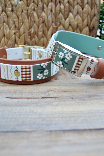 two biothane dog collars with a striping floral design and sage green accent on a wooden surface with a natural basket and plant in the backgrounds