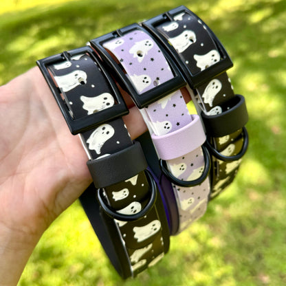 Set of dog collars with ghost print pattern held by a hand against a grassy background