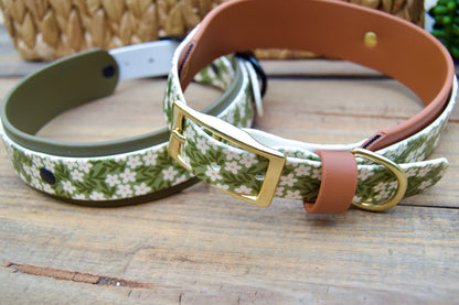 Two floral-patterned biothane dog collars on a wooden surface with a woven basket and plant in the background.