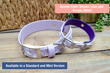 Two dog collars, one lilac and one purple, on a wooden surface with a wicker basket and plants in the background.