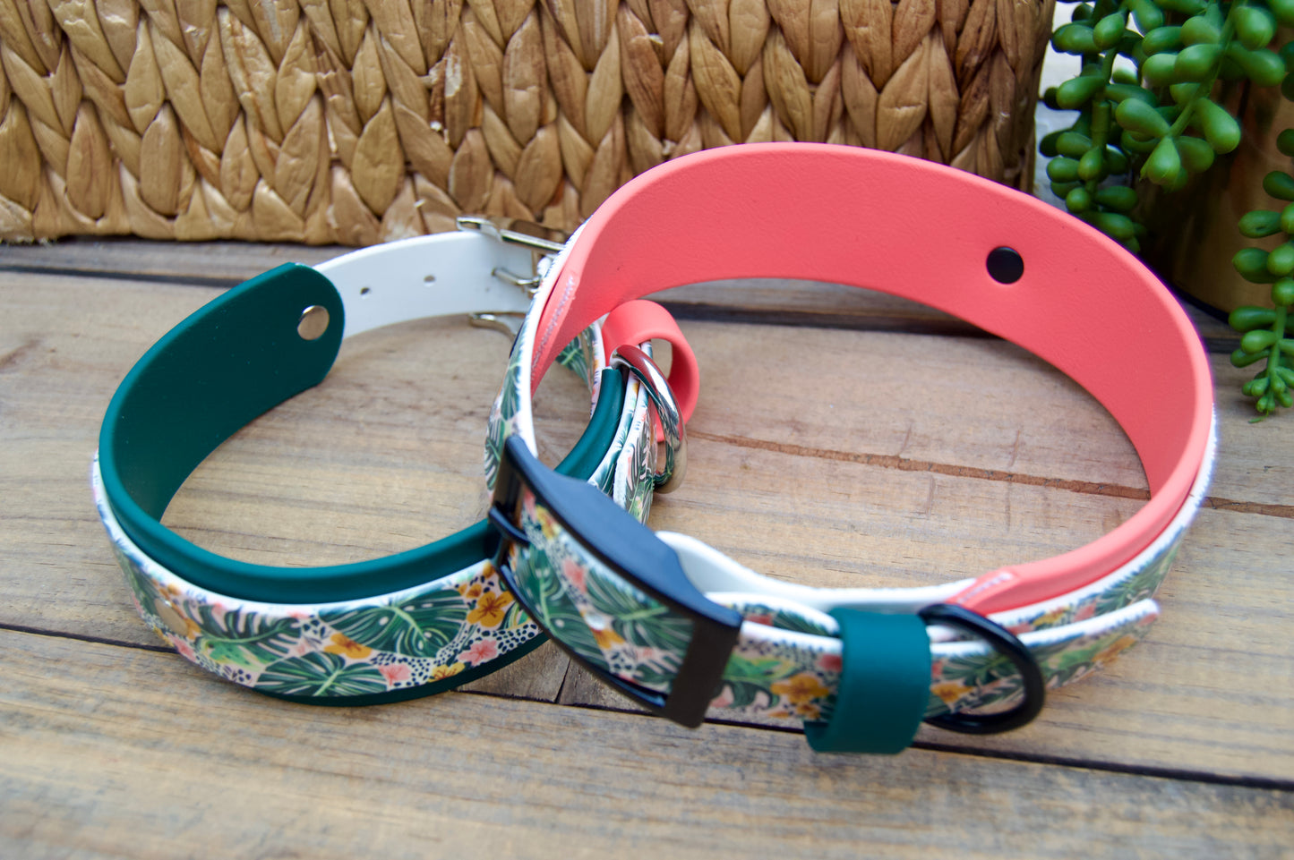 Two biothane floral-patterned dog collars on a wooden surface with a woven basket and plant in the background.